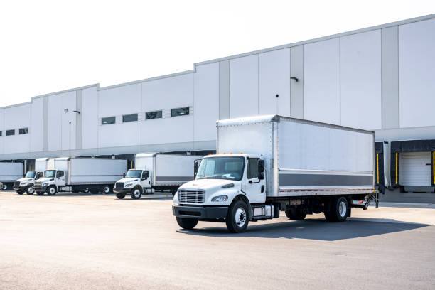 istock Huge warehouse building with docks and gates and loading cargo middle duty day cab rigs semi trucks with box trailer preparing for the next local deliveries 1703210344
