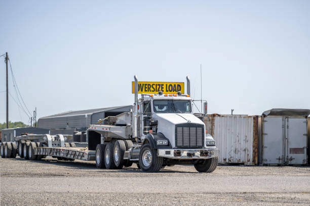 istock Oversize loader big rig powerful semi truck tractor with oversize load sign on the roof with empty step deck semi trailer standing on the industrial parking lot 1703215101