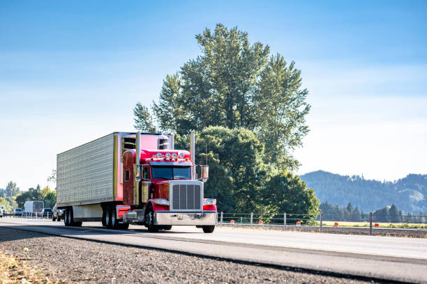 istock Popular classic bonnet American idol big rig red semi truck with extended cab transporting cargo in refrigerated semi trailer driving on the flat highway road at sunny day 1703216924