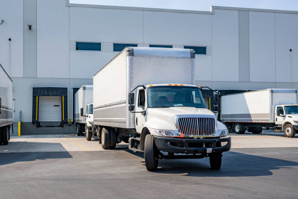 istock Maneuverable day cab middle duty rigs semi trucks with capacious box trailers standing on warehouse parking lot and in dock gates waiting for appropriate time for loading cargo for the next freight 1703221616