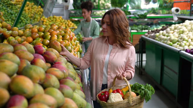 Latin American customer choosing a mango from the display at a fruit and vegetable market