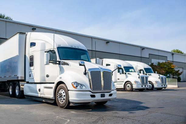 Row of the big rig semi trucks tractors with dry van semi trailers standing in warehouse docks loading cargo for the next delivery freight Industrial long hauler carriers white big rig semi trucks tractors with high cab for truck driver rest standing on the parking lot in warehouse docks gates loading cargo for the next delivery freight semi truck stock pictures, royalty-free photos & images