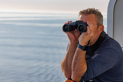 Man using binoculars from the balcony of a cruise ship enjoying the ocean views.