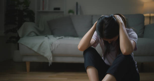 居間の床に一人で座っている悲しい落ち込んだアジアの若い女性 - 悔しい ストックフォトと画像