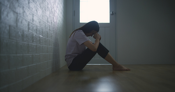 Portrait of Sad depressed young Asian woman sitting alone on the floor at home. Female lost in thoughts, suffer from psychological mental trouble. Mental health and people concept.