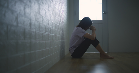 Portrait of Sad depressed young Asian woman sitting alone on the floor at home. Female lost in thoughts, suffer from psychological mental trouble. Mental health and people concept.