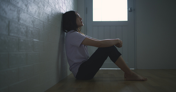 Portrait of Sad depressed young Asian woman sitting alone on the floor at home. Female lost in thoughts, suffer from psychological mental trouble. Mental health and people concept.