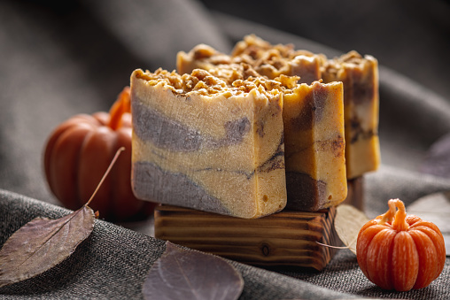 Natural soap with the aroma of pumpkin pie for a cozy autumn atmosphere on a dark background with yellow dry leaves and pumpkin shaped candles.