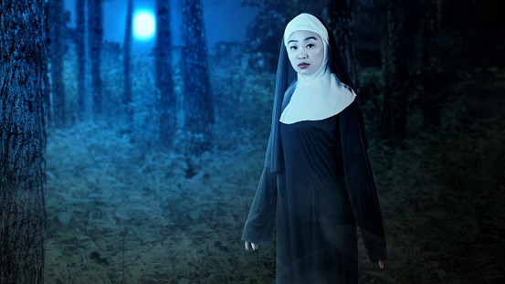 Scary devil nun standing in the misty forest in the night. Scary woman for Halloween. Halloween concept