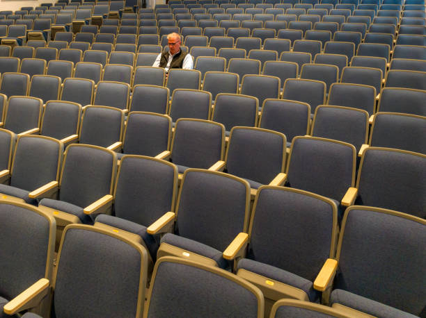 istock Overhead view a middle age man with gray hair sitting alone in an empty, auditorium seats, chairs. 1703353169