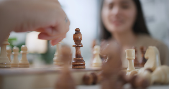 selective focus,  young woman moving pieces on chess board during competition with friend, they are talking and smile with fun during challenge in chess game together