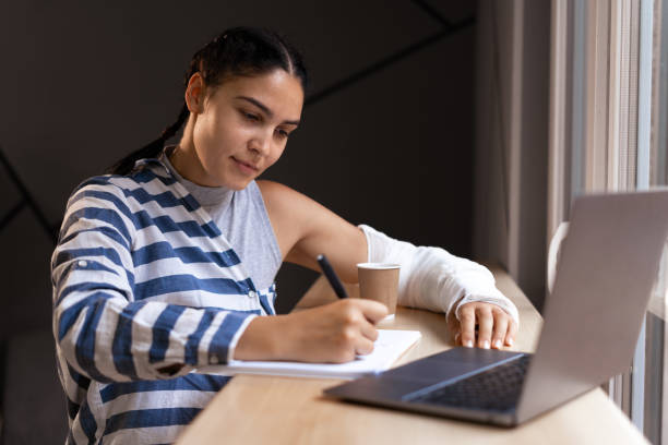 istock Concentrated female student writing in notebook while learning with cardboard coffee cup in coffee shop, doing remote job via laptop computer 1703451710