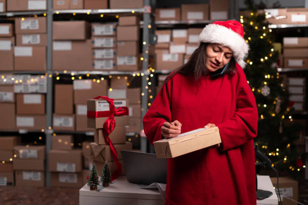 istock Drop-shipping business owner talking on mobile phone and taking order working in small warehouse. Female entrepreneur with box at storage office confirming the order on phone. 1703452074
