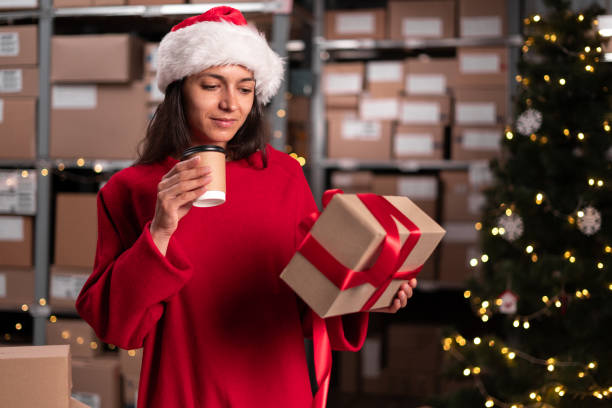 istock Female inventory manager worker working on Christmas Eve holding cardboard box. Parcels with products ready for shipment on stock. 1703452086