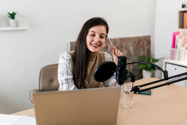 istock Young smiling woman recording podcast and doing live streaming using microphone and headphones in recording studio 1703463436