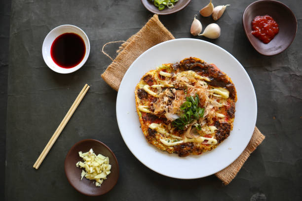 okonomiyaki, pizza tradizionale giapponese, pizza giapponese con piastra calda di okonomiyaki. fatto di farina che viene diluita con acqua o dashi, più cavolo, uova di gallina, frutti di mare e fritti in un teppan - okonomiyaki foto e immagini stock