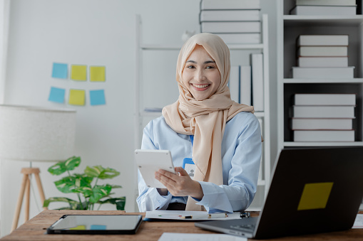 Female company employee wearing a hijab works in the office, auditing the company's accounts and finances to ensure the accuracy and safety of finances. Concepts of working in finance and accounting.