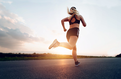 Mujer deportiva corriendo al atardecer en la carretera. Concepto de salud, adelgazamiento y mantenimiento de la juventud photo
