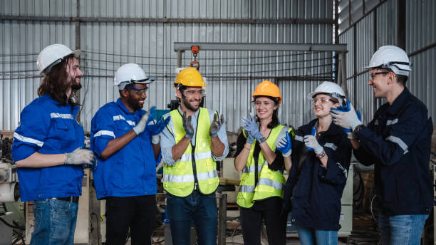 istock Team engineers and foreman stack hand and shake hands to show success at factory machines. Workers are controlling welding robots. 1703554608