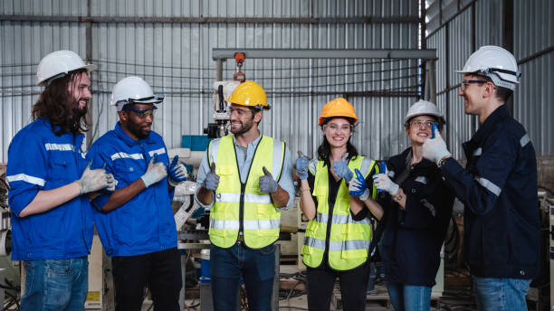 istock Team engineers and foreman stack hand and shake hands to show success at factory machines. Workers are controlling welding robots. 1703555135