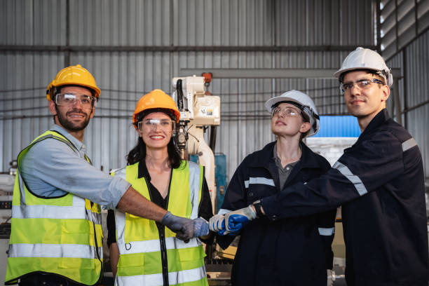 istock Team engineers and foreman stack hand and shake hands to show success at factory machines. Workers are controlling welding robots. 1703555709