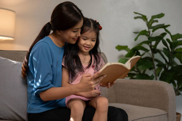 istock A happy and caring young Asian mom is embracing her daughter while reading a book on a couch. 1703556867