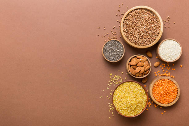 varios superalimentos en tazón pequeño sobre fondo de color. superalimentos como arroz, chía, quinoa, lentejas, nueces, semillas de sésamo, almendras. espacio de copia de vista superior - quinoa sesame chia flax seed fotografías e imágenes de stock