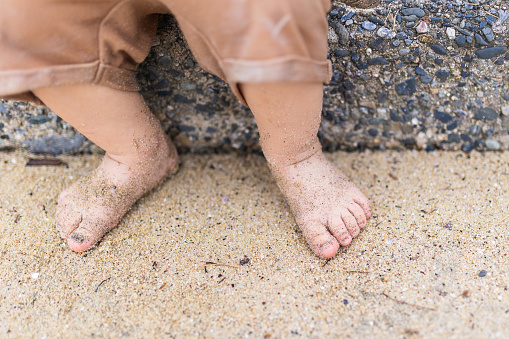 A young toddler sitting on steps at the beach, close up of his cute little sandy feet.