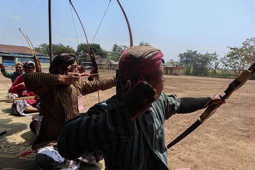 Klaten, Indonesia, august 15, 2023. male and female participants, dressed in Javanese custom pulled his bow by squinting to achieve concentration of target accuracy in traditional Javanese arrow trad