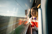 A happy little girl with curly hair is looking through the window while traveling by train