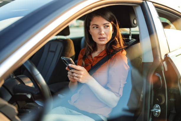 ritratto di una giovane donna che invia messaggi sul suo smartphone mentre guida un'auto. donna d'affari seduta in auto e usando il suo smartphone. autista femminile e schermo del telefono - car phone foto e immagini stock