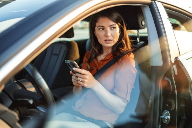 портрет молодой женщины, пишущей текстовые сообщения на свой смартфон во время вождения автомобиля. деловая женщина сидит в машине и испол� - car phone стоковые фото и изображения