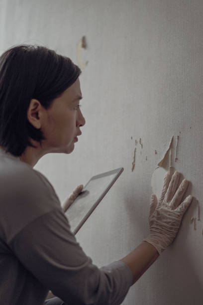 istock Woman looks at broken wallpaper 1703681295