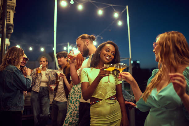 istock Stylish young people, friends meeting in evening outdoors, on rooftop, drinking, talking, having fun together 1703691672