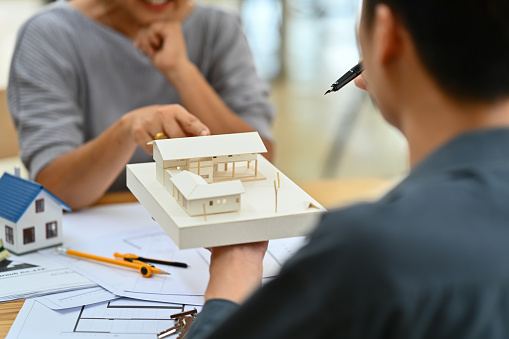 Over shoulder view of architect man showing house model, explaining house renovation plan with client.