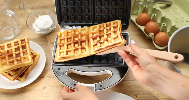 istock Women's hands take out cooked waffles from electric waffle iron. 1703711472