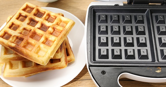 Cooked waffles and waffle iron. Food preparation.