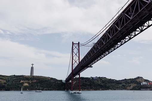 Landscape view on the 25th of April Bridge in Lisbon city, Portugal. Low angle view. The Sanctuary of Christ the King, Santuario de Cristo Rei in the background.