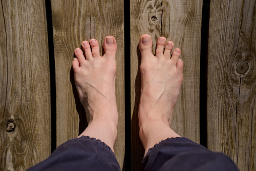 Image of bare female feet standing on wooden surface with toes splayed top view closeup