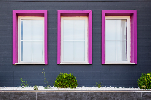 Three windows on grey wall with purple or pink frames, modern exterior design