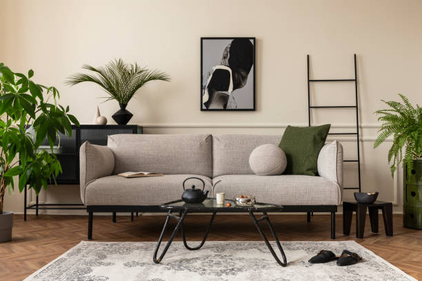 istock Creative composition of living room interior with mock up poster frame, gray sofa, black coffee table, patterned rug, plants in flowerpots, slippers and personal accessories. Home decor. Template. 1703792611