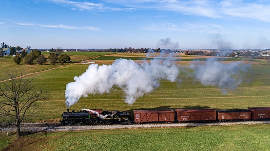 Ronks, United States – November 07, 2021: An Aerial Side View of a Steam Freight Train Traveling Thru Farmlands Blowing Smoke on a Sunny Autumn Day