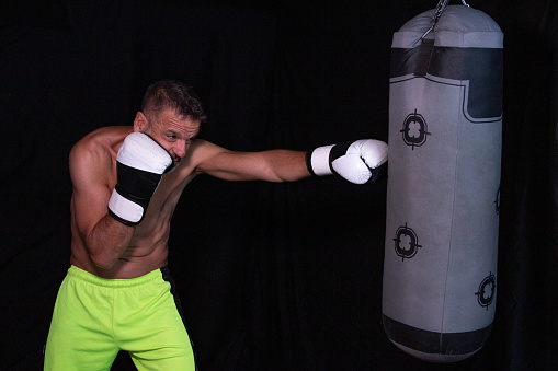 Mature man boxing, hitting a punching bag, shirtless on a black background