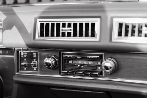The dashboard controls of a vehicle, with the radio dials clearly visible, in grayscale