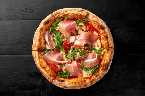 Pizza with salami, prosciutto, tomatoes, mozzarella and fresh arugula stock photo
