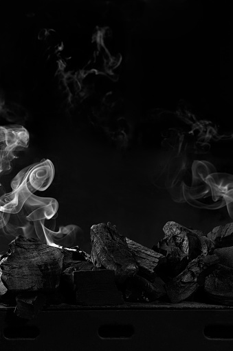 Closeup of extinguished coals on metal grill barbecue on black background with light white smoke. Vertical image with copyspace