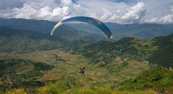 Against background of blue summer cloudy sky, tandem of paragliders flies on red ultralight aircraft - paraglider. Extreme sport and recreation.