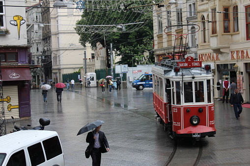 Tünel Square, at the end of Istiklal Street. A view from the entrance of the funicular. People in their daily lives on a rainy day. Right next to the Swedish consulate. The historical tram is nearing the end of the stop.