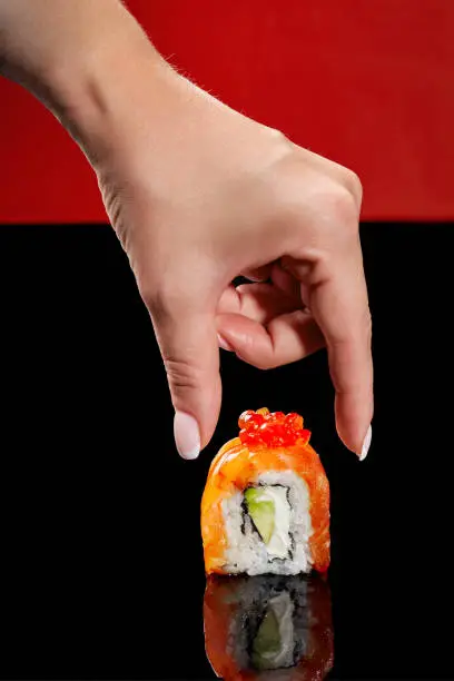 Photo of Female hand reaching out to Philadelphia sushi roll with salmon, cream cheese, avocado and red caviar