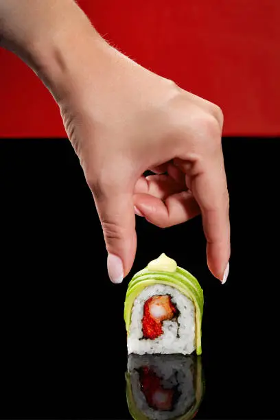 Photo of Female hand taking sushi roll with shrimp, flying fish roe, avocado and Japanese mayonnaise